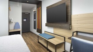 Een hotelkamer met een bed, bureau, bankje, televisie en een douche.