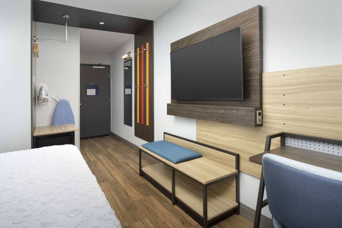 Een hotelkamer met een bed, bureau, bankje, televisie en een douche.