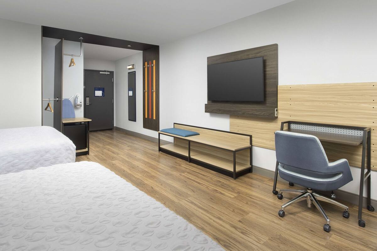 Een hotelkamer met twee bedden, een bureau, een stoel, een televisie en een houten hoofdeinde.