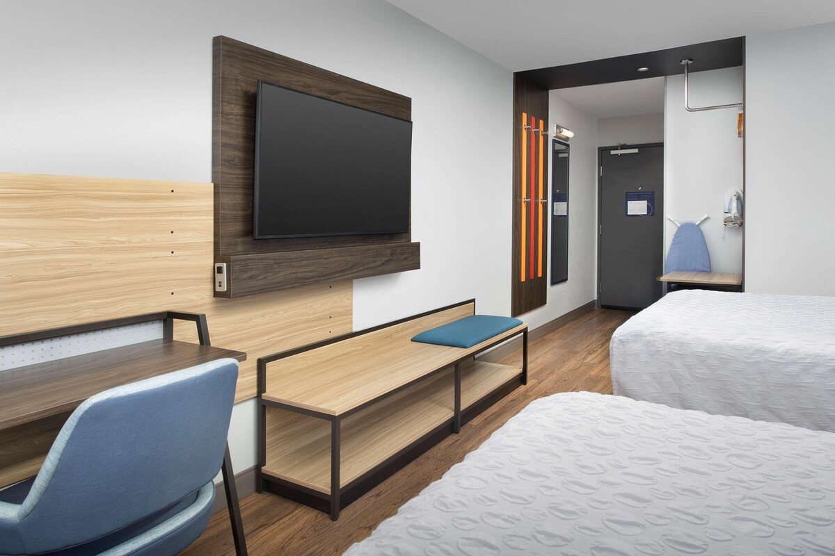 Une chambre d’hôtel comprenant un lit, un bureau avec une chaise, un téléviseur fixé au mur et une porte donnant accès à une salle de bain.