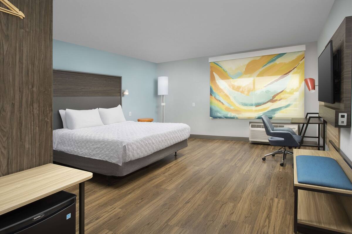 Een moderne hotelkamer met een bed, bureau, stoel en een groot abstract schilderij aan de muur.