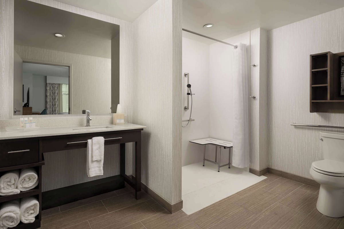 A modern bathroom with a large mirror, dark vanity, white towels, a shower area, and a toilet.