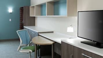 A modern hotel room with a desk, chair, television, and built-in shelving.