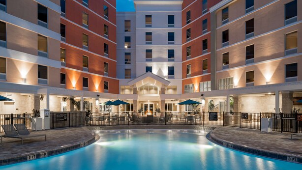 A hotel with a central swimming pool, multiple floors, and outdoor seating areas. - Home2 Suites by Hilton Cape Canaveral Cruise Port, FL (Cape Canaveral)