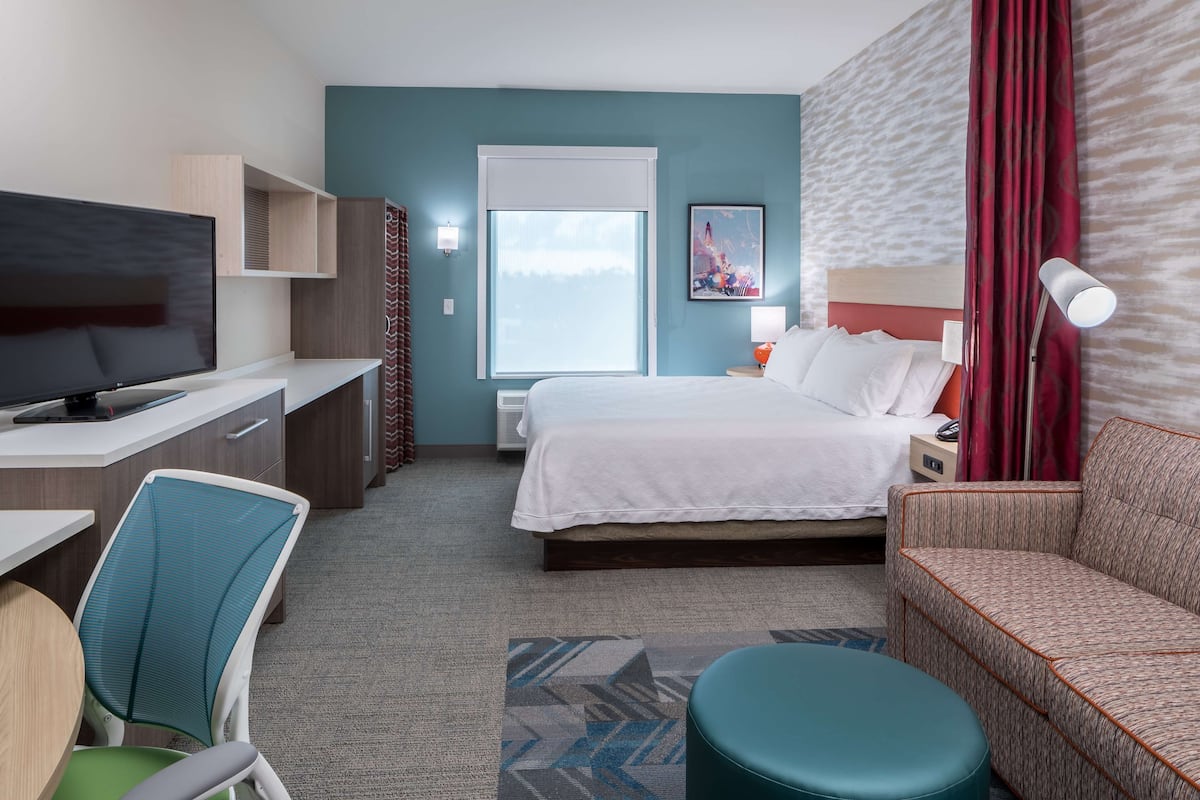 Une chambre d’hôtel comprenant un lit, un bureau avec une télévision, une chaise, un canapé et une fenêtre avec des rideaux.