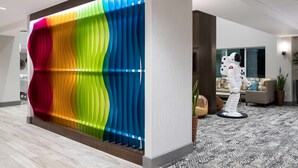 A modern interior with a colorful, wavy partition, a white astronaut statue, and a patterned carpet. - Home2 Suites by Hilton Cape Canaveral Cruise Port, FL (Cape Canaveral)