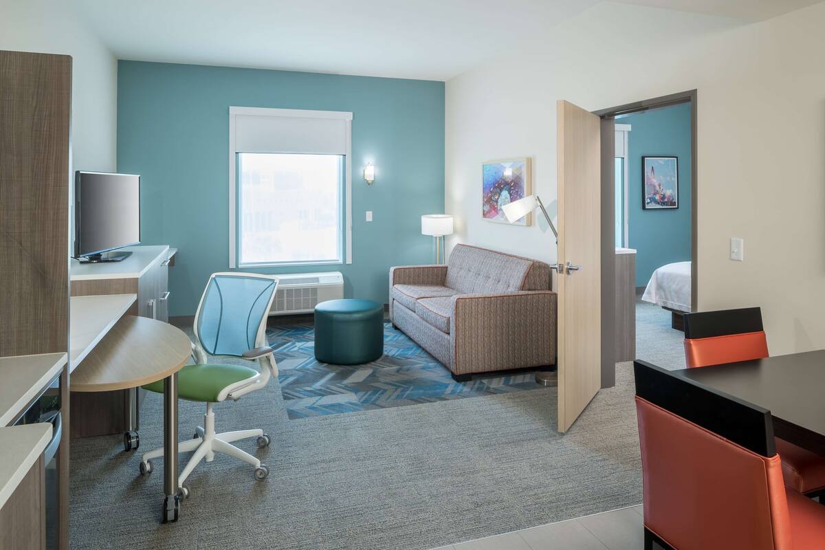 Une chambre d’hôtel moderne équipée d’un bureau, d’une chaise, d’un canapé, d’un pouf et d’un lit.