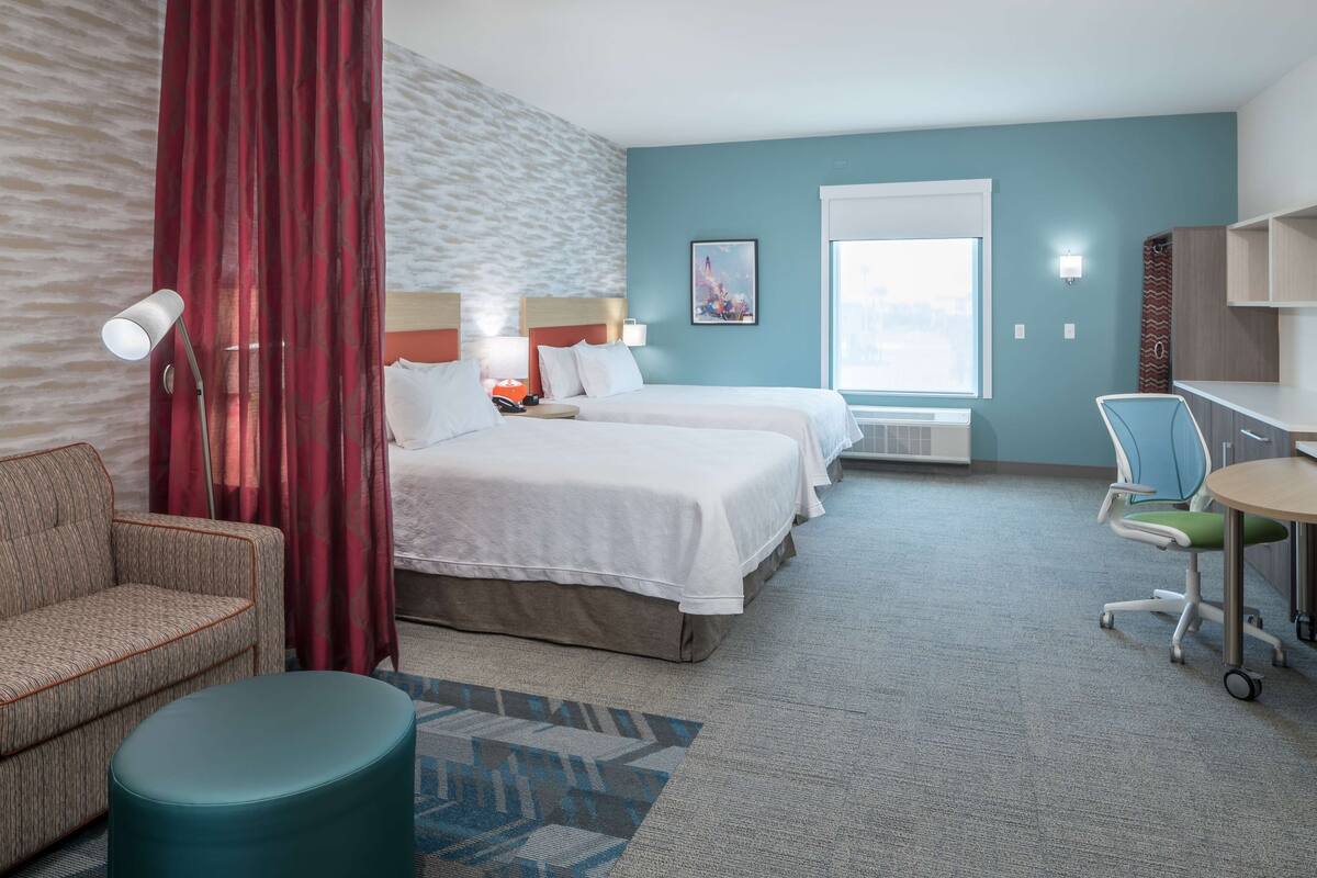 Une chambre d’hôtel avec deux lits, un bureau, une chaise, une lampe et une fenêtre.