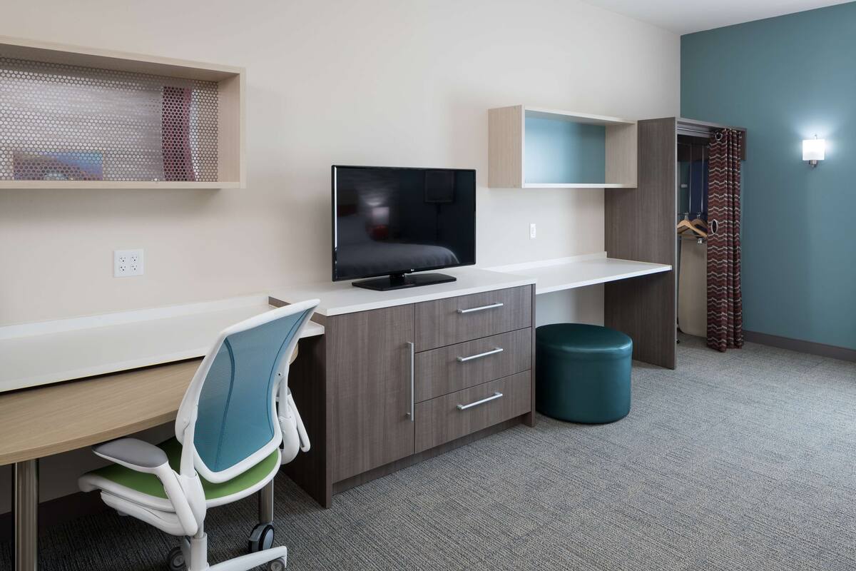 Une chambre d’hôtel moderne équipée d’un bureau, d’une télévision et d’une armoire.