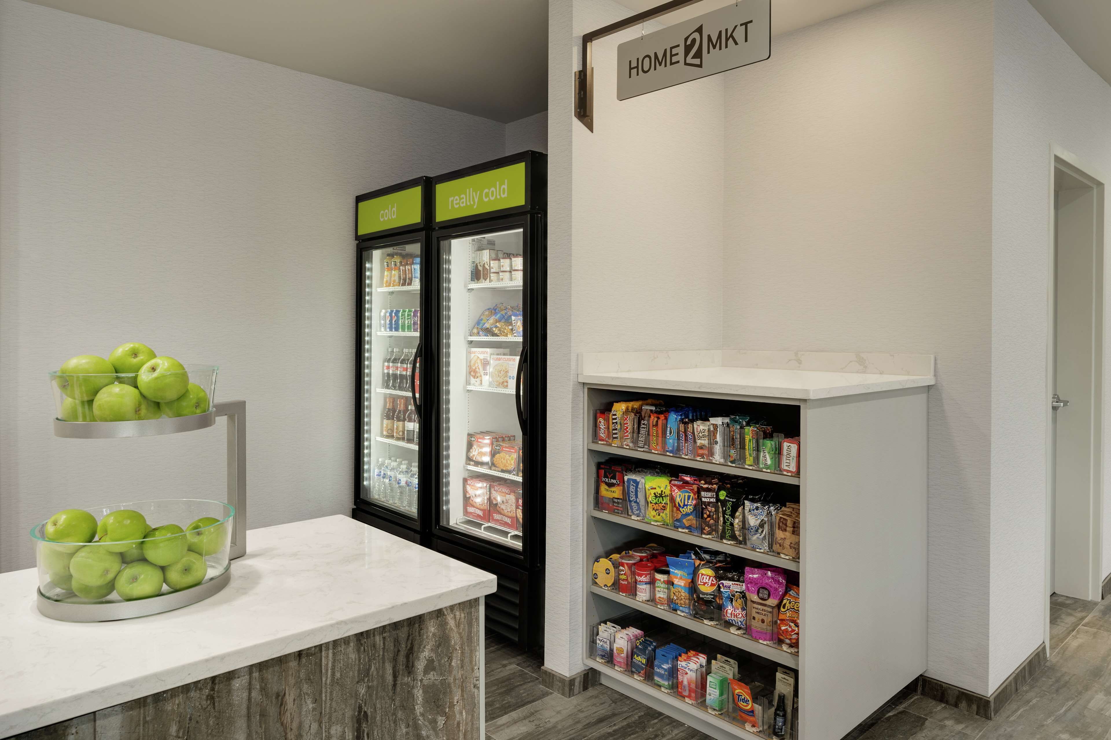 Una kitchenette con encimera de mármol, una presentación de frutas, un refrigerador con etiquetas que dicen 'frío' y 'muy frío', y una alacena con diversos alimentos.