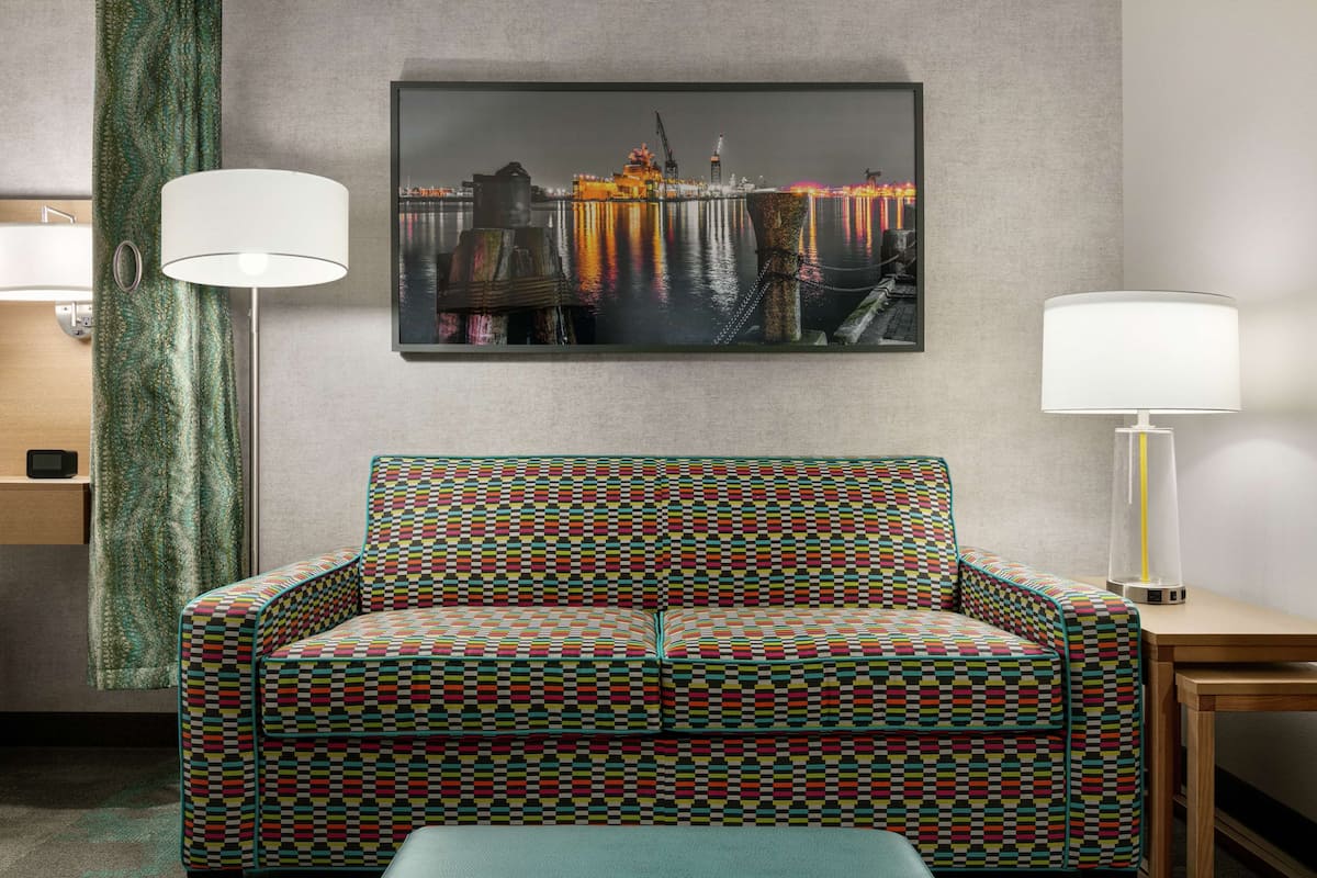 Ein gestreiftes Sofa, ein gerahmtes Stadtbild und zwei Stehlampen in einem Hotelzimmer.