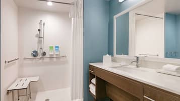 Un baño moderno con ducha, tocador con espejo y un taburete pequeño.