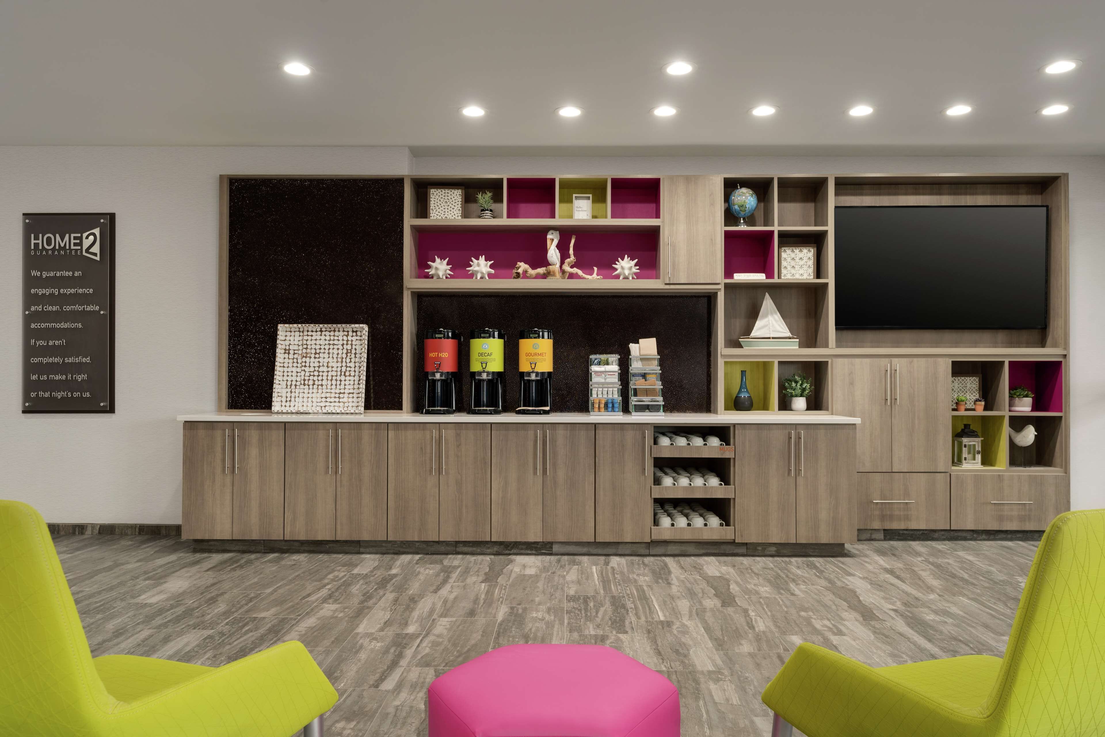 A modern hotel lobby with a wooden reception desk, a large flat-screen TV, and bright green chairs.