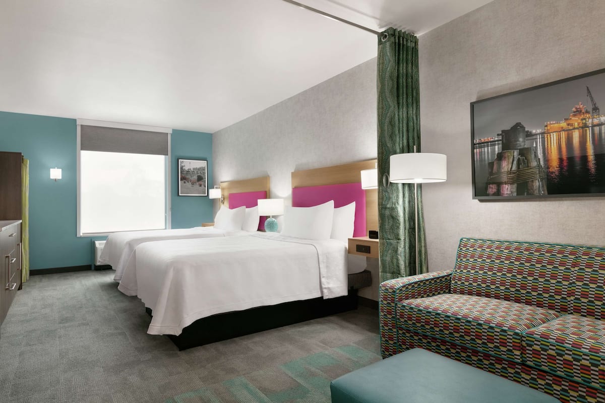 Ein Hotelzimmer mit zwei Betten, einer Couch, einem Schreibtisch und einem Fenster.