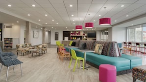 Um interior moderno com um sofá verde-esmeralda, cadeiras coloridas e um banquinho rosa vibrante.