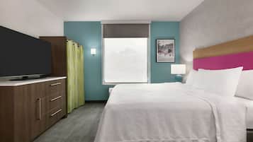 Habitación de hotel con cama, televisor en un mueble de madera, ventana con vistas y un cuadro en la pared.
