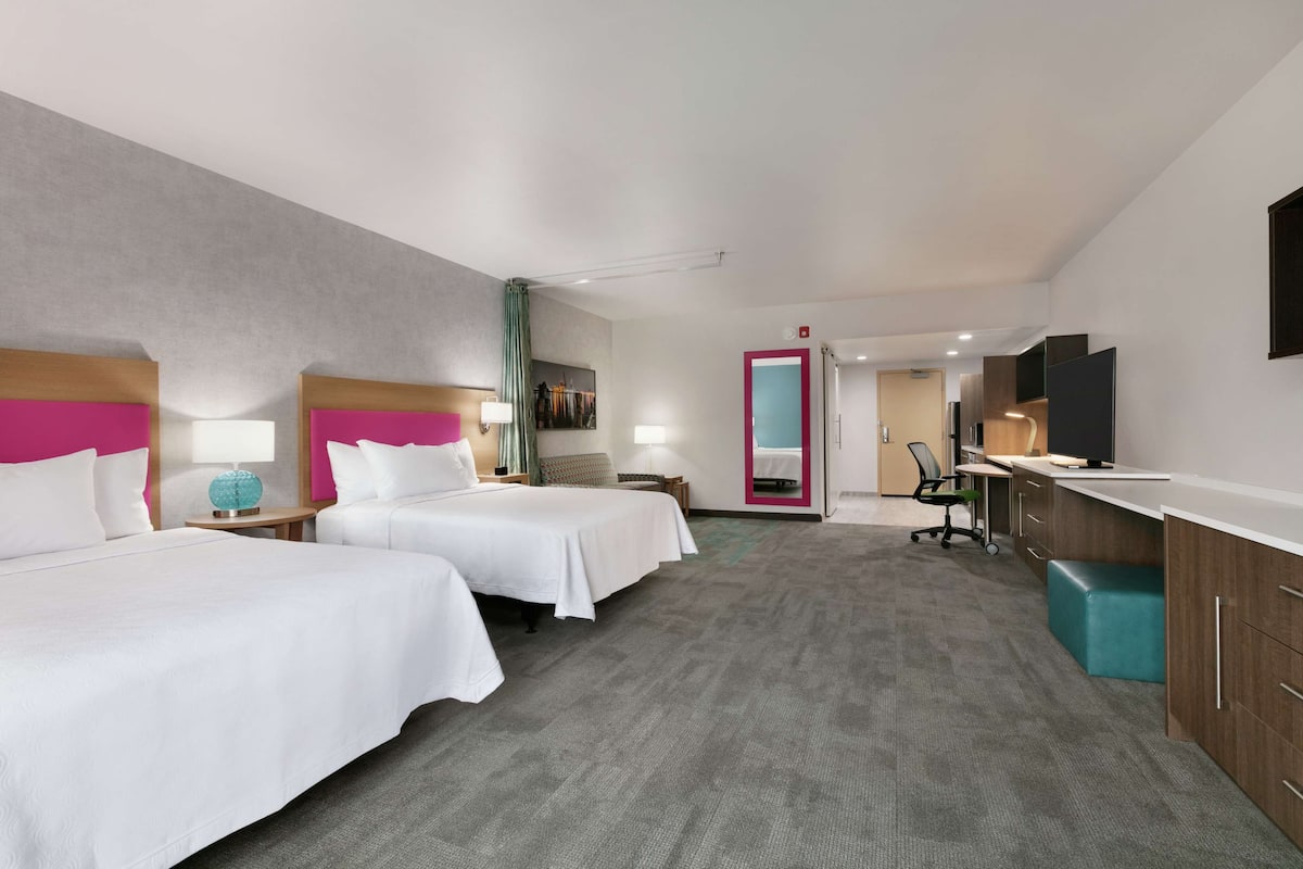 Ein Hotelzimmer mit zwei Betten, einem Schreibtisch, einem Sessel, einem Fernseher und einem Spiegel.