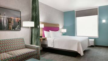 Habitación de hotel con cama, sofá estampado, ventana grande y cuadro de paisaje urbano en la pared.