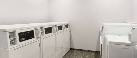 A laundry room with multiple white washing machines and dryers, a tiled floor, and white walls.