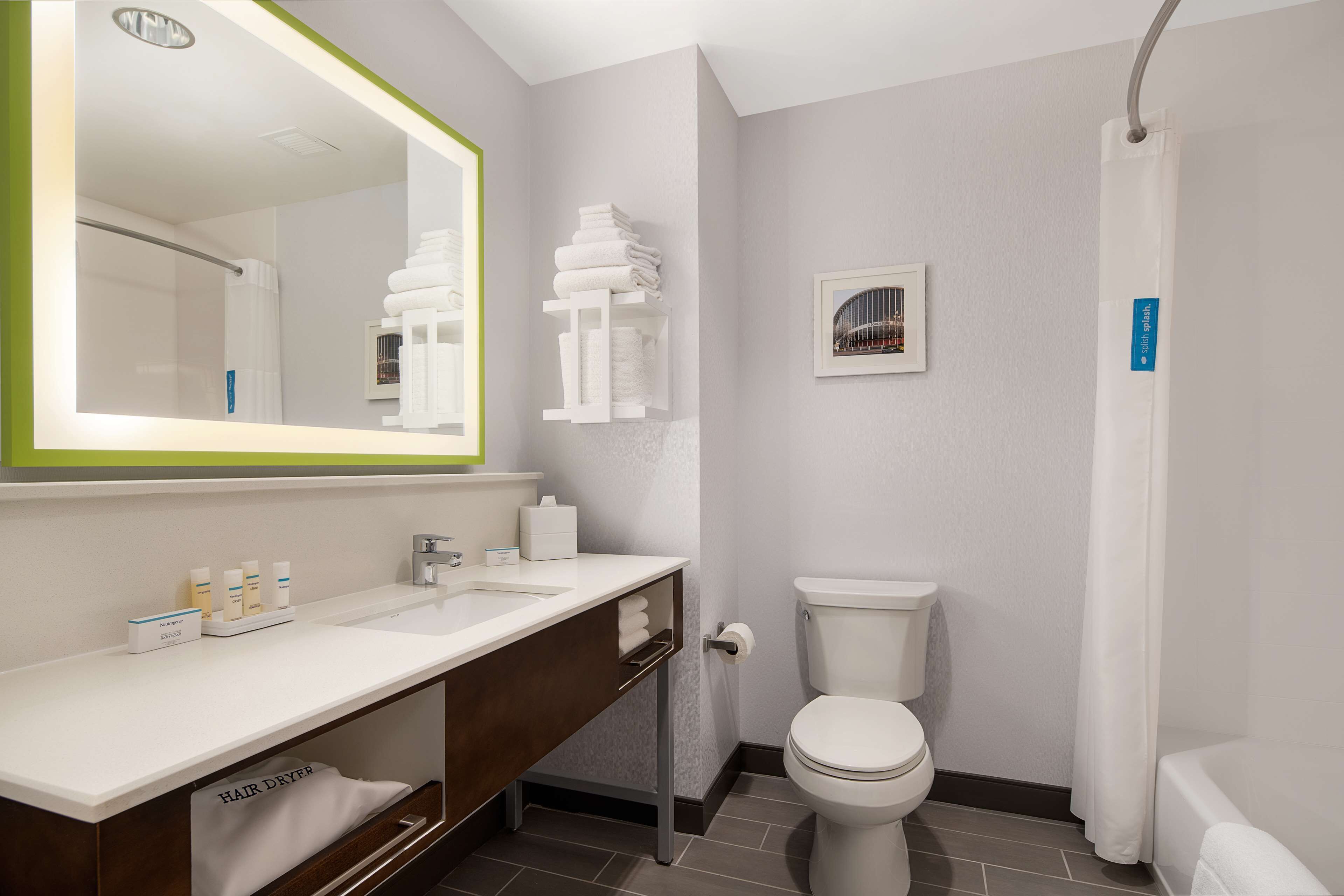 A modern bathroom with a large mirror, dual sinks, a toilet, and a shower area.