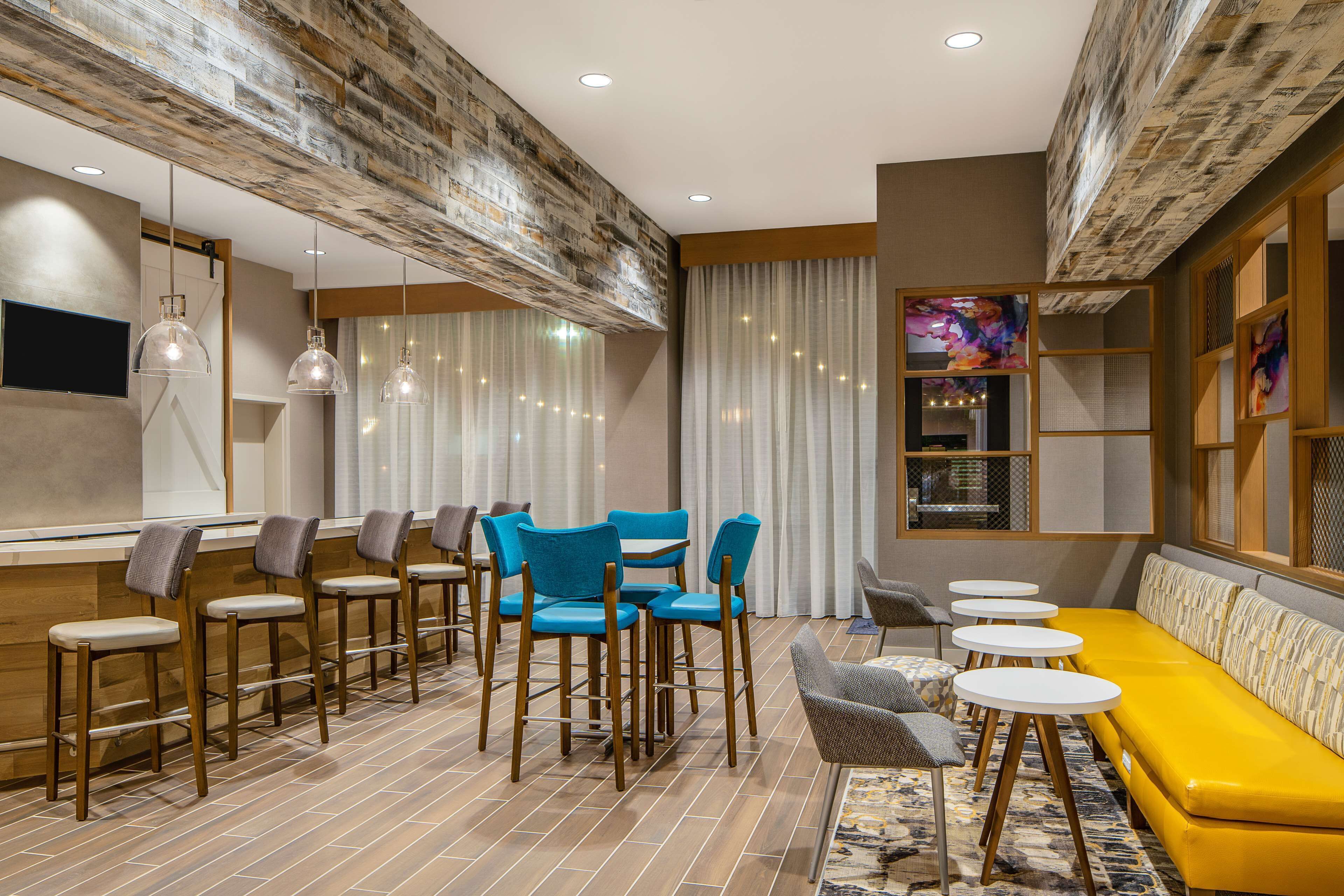 A modern lounge area with bar stools, a yellow sofa, and a TV mounted on the wall.