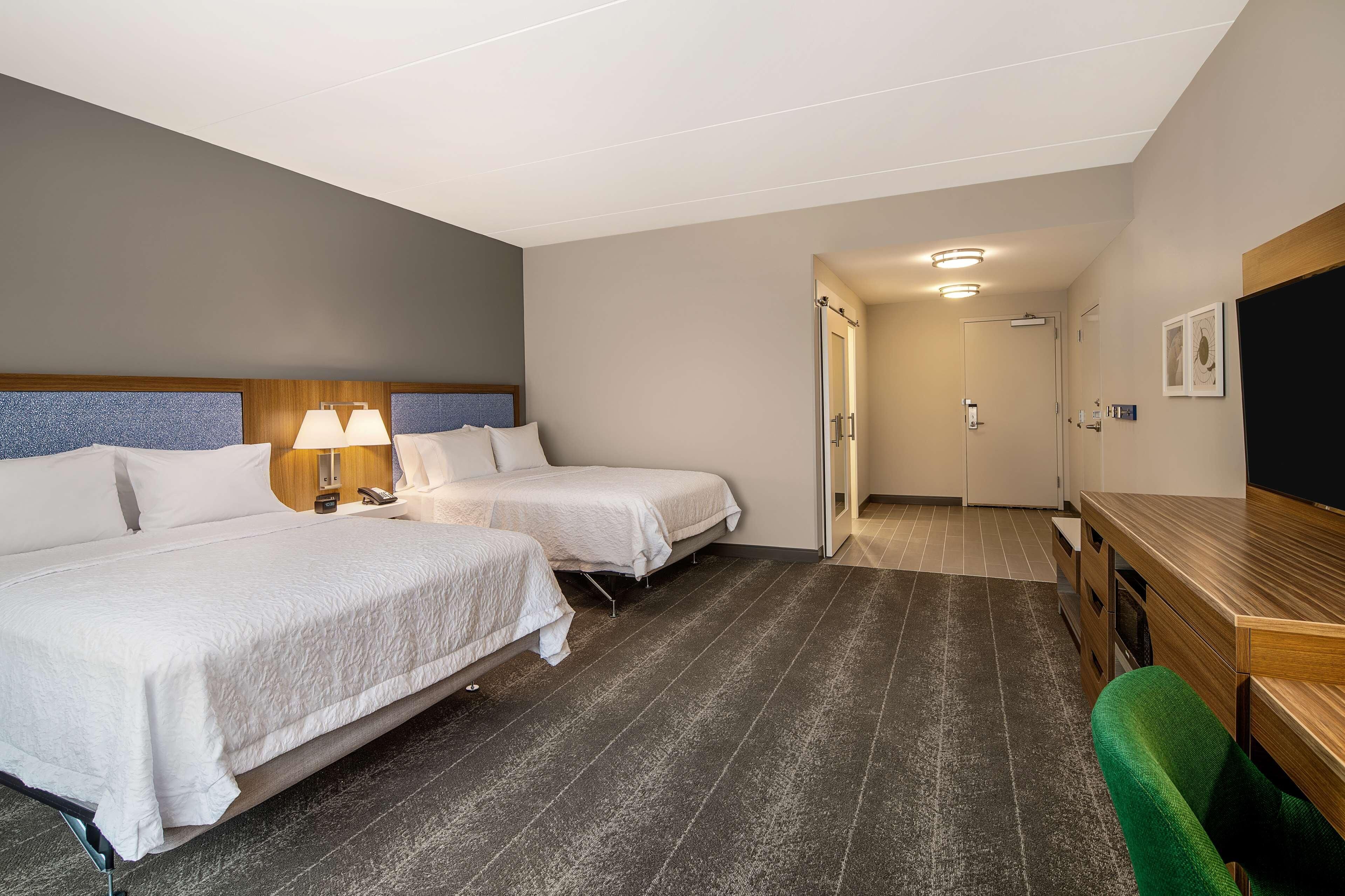 A hotel room with two beds, a desk, a chair, and a door leading to a bathroom.