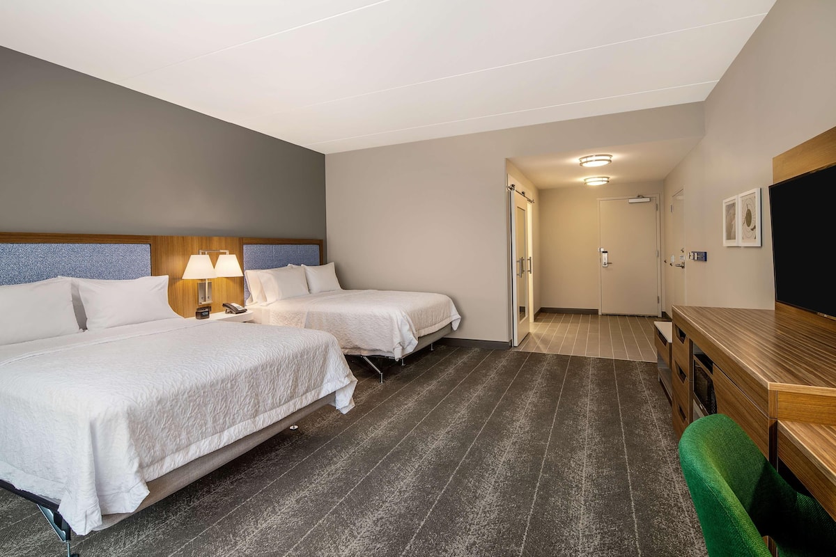 A hotel room with two beds, a desk, a chair, and a door leading to a bathroom.