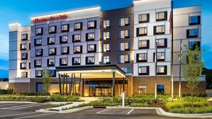 Un hotel Hampton Inn & Suites con una fachada moderna, varios pisos y una entrada bien iluminada.