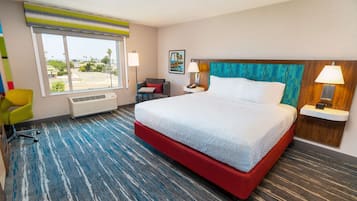 A hotel room with a large bed, a desk, a chair, and a window with a view of the outside.