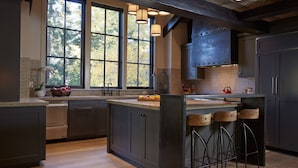 A modern kitchen with large windows, dark cabinetry, and a central island with bar stools. - Stunning Private Compound with Hot Tub, Nearby Beach, Flat Lawn, at ski resort (Homewood)