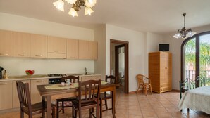A kitchen with wooden cabinets, a dining table with chairs, a TV on a cabinet, and a bed with a window view. - Experience Italian flair up close - Monolocale 900 (Racale)
