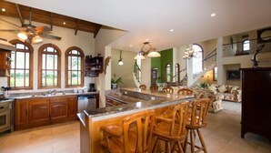 Une cuisine spacieuse avec des meubles en bois, un grand îlot central doté de tabourets, et un coin repas avec un canapé et des chaises.