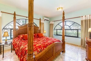 A four-poster bed with a floral bedspread, a wooden headboard, and a nightstand with a lamp.