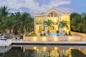Une maison moderne avec une piscine, des palmiers et un bateau amarré au bord de l’eau.