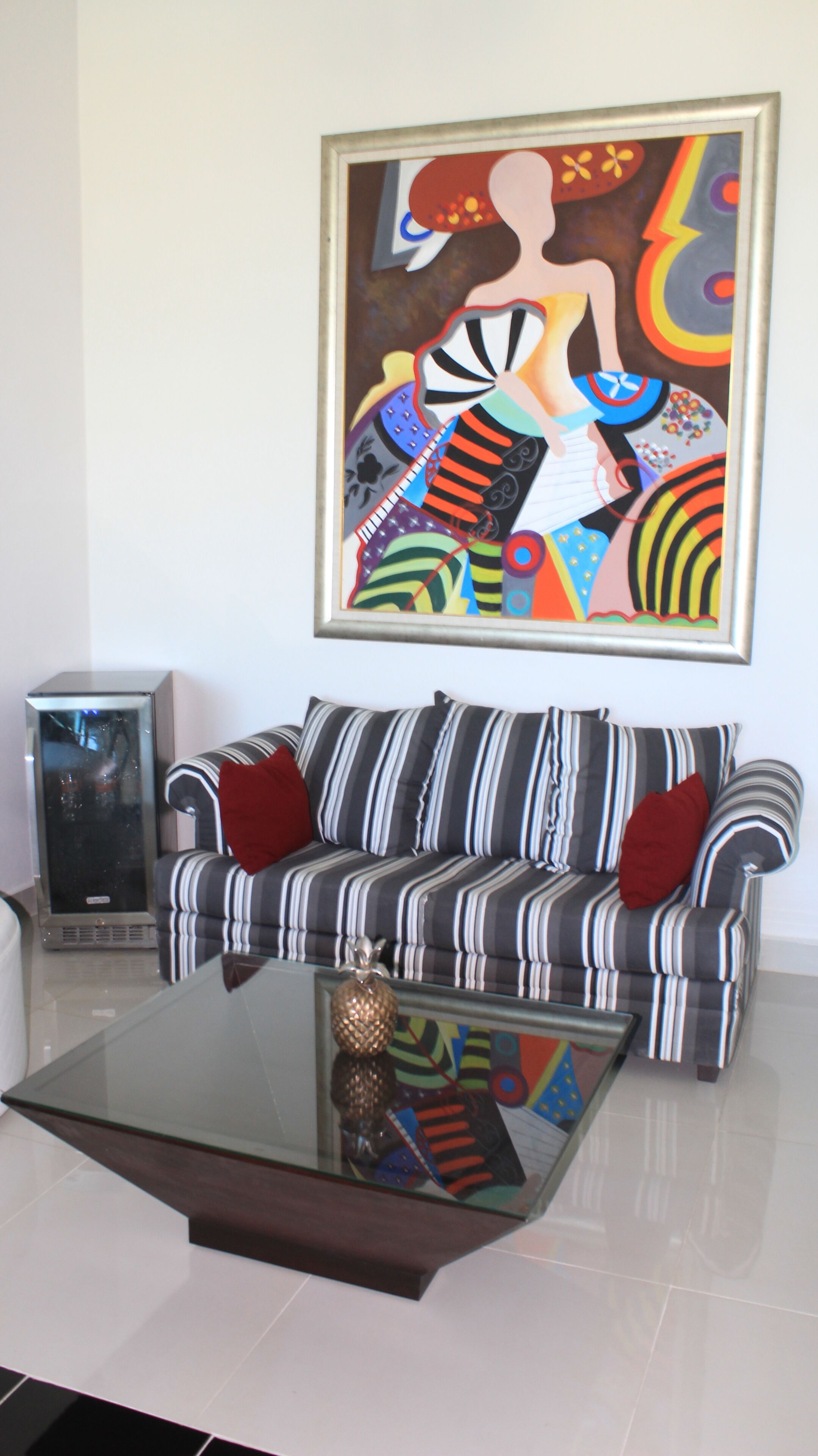 Un salon avec un canapé à rayures, une table basse en verre et un tableau abstrait aux couleurs vives accroché au mur.