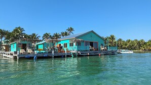 Un edificio turquesa con un letrero que dice "Restaurant Bar" sobre un muelle que se adentra en aguas cristalinas, rodeado de palmeras.