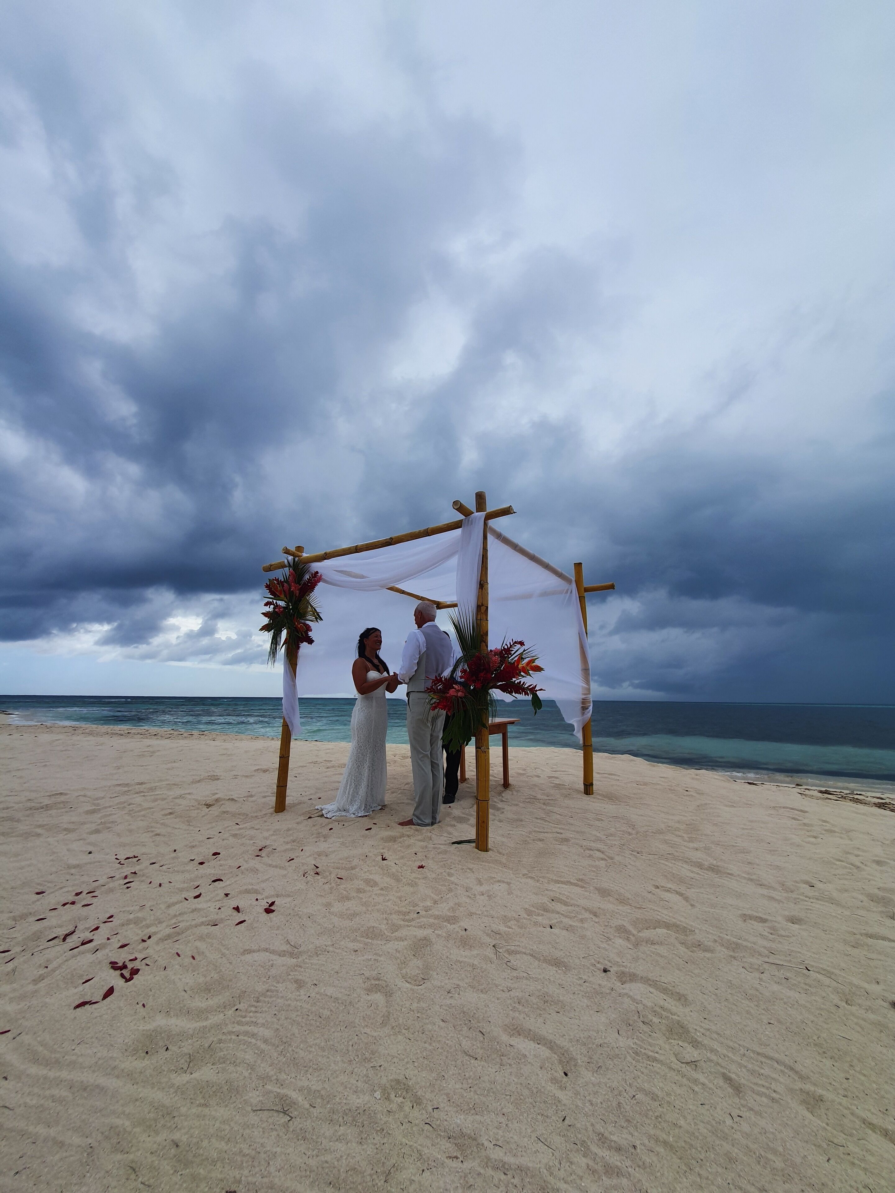 Una cerimonia nuziale sulla spiaggia, con un semplice arco di legno e decorazioni floreali.