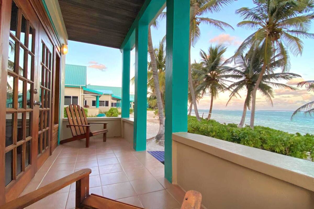 A covered porch with a view of the ocean and palm trees.