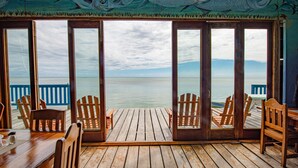 Una terraza de madera con sillas y una mesa, amplias puertas de cristal con vistas al mar.