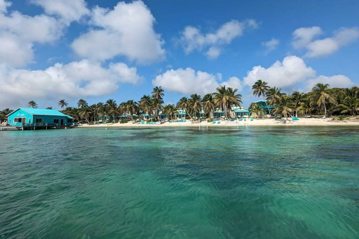 A beachfront property with a turquoise building, palm trees, and clear blue waters.