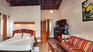 Un dormitorio con cama, mesitas de noche, cabecero de madera, sofá y una zona de cocina con microondas y armarios.