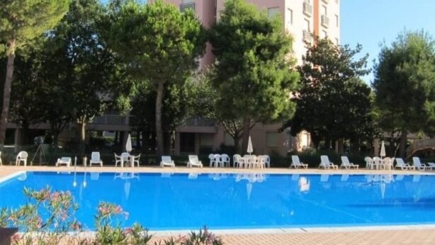 Una piscina rodeada de árboles y sillas de descanso blancas.