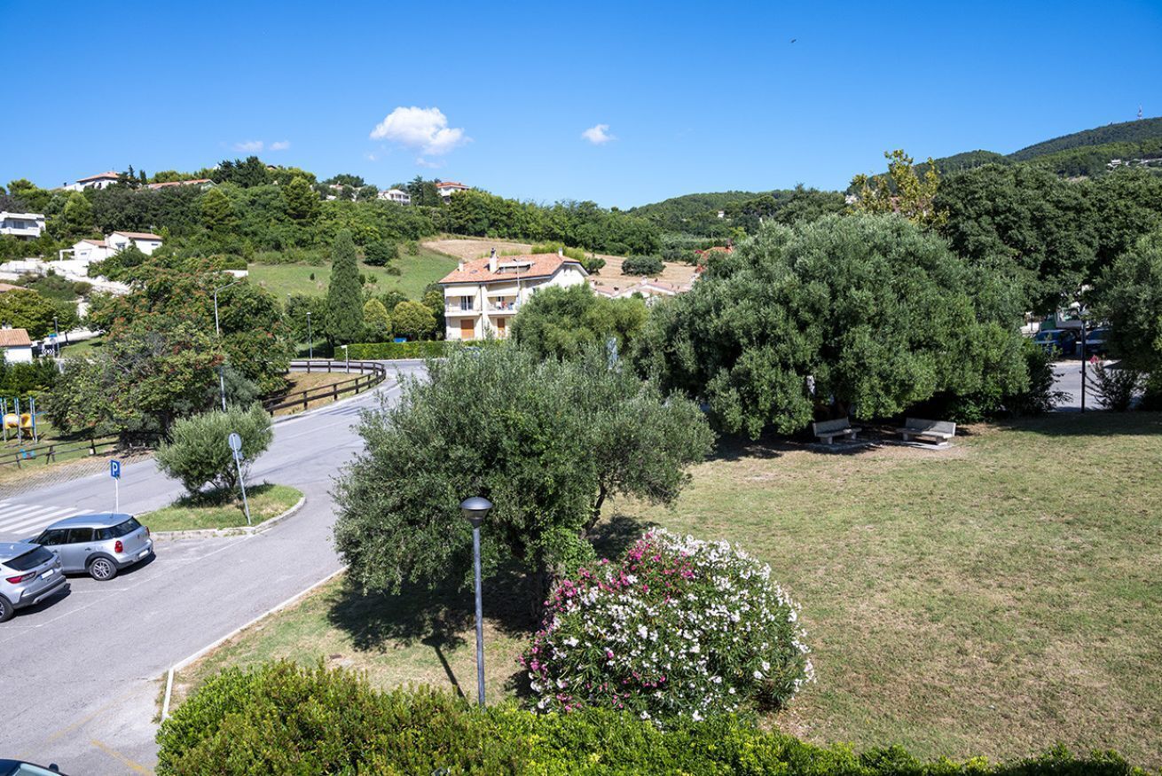 A residential area with houses, a curved road, and a grassy hill with trees.