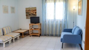 A living room with a striped sofa, a blue sofa, a TV on a wooden stand, and a painting on the wall. - S220 - Sirolo, three-room apartment in the center with terrace (Sirolo)