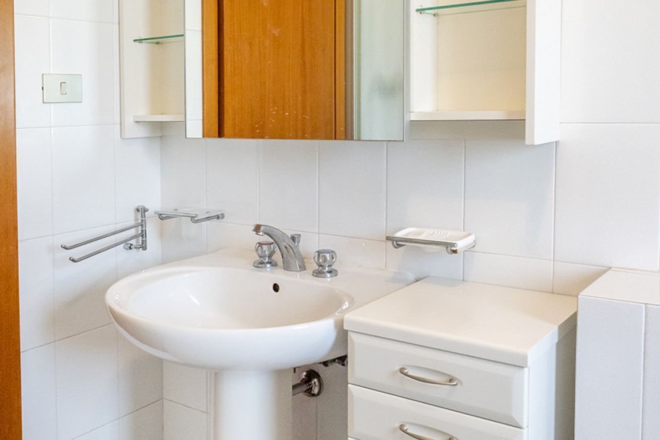 A bathroom with a white sink, a wooden cabinet, and a mirror.