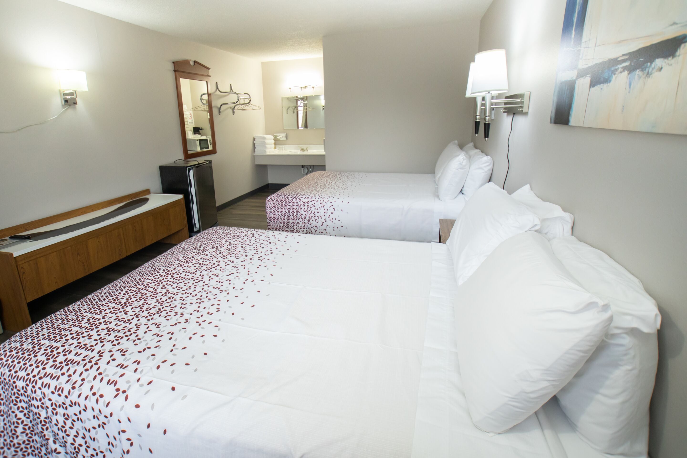 Habitación de hotel con dos camas, un escritorio, un espejo y un baño a la vista.