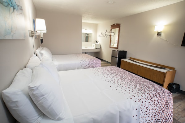 A hotel room with two beds, a wooden headboard, a small desk, a mirror, and a wall-mounted lamp.