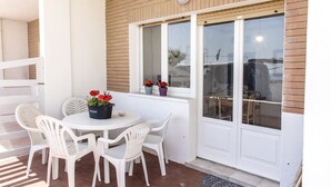 Eine Terrasse mit einem runden Tisch und weißen Stühlen, ein Fenster mit Ausblick sowie eine Tür mit Glasverkleidung.