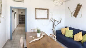 Ein Essbereich mit einem Holztisch, Stühlen, einer Topfpflanze, einem blauen Sofa mit Kissen, einer Pendelleuchte und einem an der Wand befestigten Bilderrahmen.