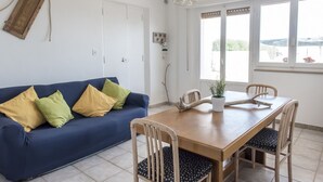 Ein Zimmer mit einem blauen Sofa, einem Holzesstisch, Stühlen, einer Topfpflanze und einer Pendelleuchte.